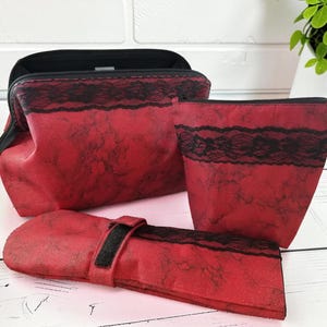 Pode incluir: Um conjunto de três bolsas de cosméticos vermelhas com um padrão de mármore preto e um detalhe de renda preta. A coleção inclui uma bolsa grande aberta, uma bolsa menor com zíper e um estojo longo, plano e retangular com fecho de velcro.
