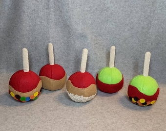 May include: Five felt apple ornaments, each with a different topping. Two are red with brown caramel, one is red with colorful sprinkles, and two are green with red caramel and colorful sprinkles.