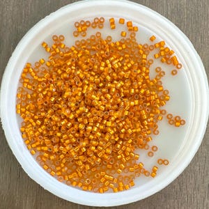 May include: A white bowl filled with small, shiny, orange seed beads.