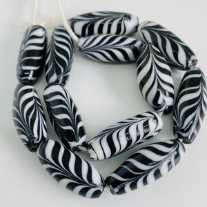May include: A strand of black and white glass beads with a swirl pattern. The beads are oval shaped and have a glossy finish.
