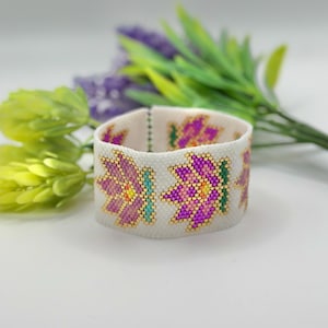 May include: White beaded bracelet with a floral design featuring pink, purple, green, and gold beads.