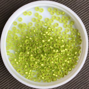 May include: A container filled with small, round, lime green glass beads. The beads have a metallic gold finish.