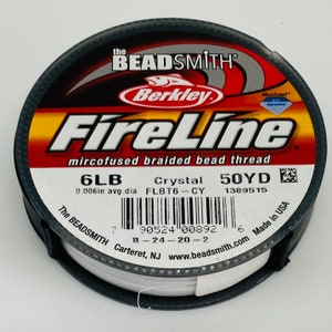 May include: A white spool of 6lb Berkley FireLine microfused braided bead thread in a crystal color. The spool is labeled with the brand name, product name, and details like the line diameter, color, and yardage. The spool is also labeled with a barcode and the words "Made in USA".