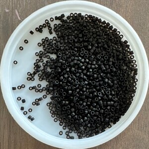 May include: A white bowl filled with black seed beads. The beads are small and round, and they are scattered randomly in the bowl.