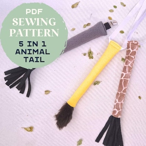 May include: A PDF sewing pattern for five animal tails. The tails are in various colors and patterns, including gray, yellow, brown with giraffe print, and black. Each tail has a white ribbon attached. The text "PDF SEWING PATTERN 5 IN 1 ANIMAL TAIL" is in a green circle.