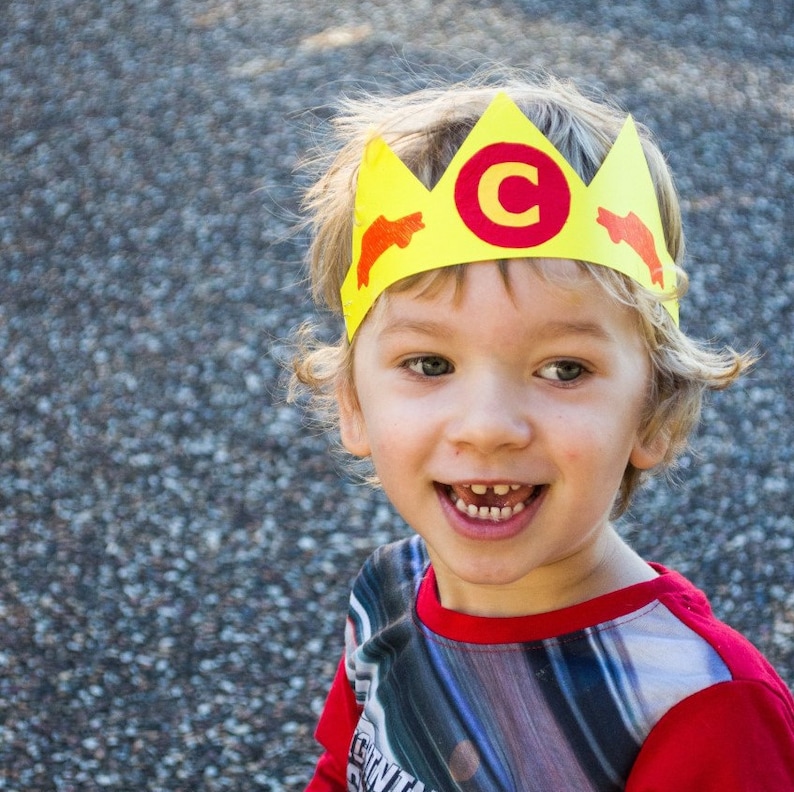 Puede incluir: Un ni&ntilde;o peque&ntilde;o con una corona de papel amarilla con una C roja y dise&ntilde;os de peces naranjas. El ni&ntilde;o sonr&iacute;e y lleva una camisa a rayas rojas y grises.