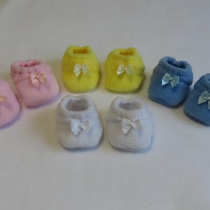 May include: Six pairs of baby booties in different colours: pink, yellow, blue, and white. Each bootie has a small bow on the top.