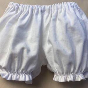May include: White cotton baby bloomers with a ruffled edge.
