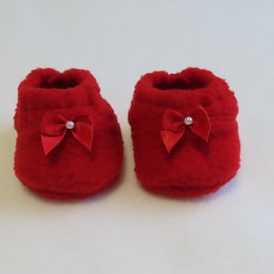 Peut inclure: Une paire de chaussons de bébé rouge vif. Chaque chausson a un nœud en satin avec un accent de perle. Les chaussons sont faits d'une matière douce et duveteuse. Ces chaussures de bébé sont parfaites pour un nouveau-né.