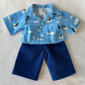 Peut inclure: Un ensemble deux pièces pour poupée. La chemise bleu clair est ornée d'un motif de pingouins et d'icebergs, avec des manches courtes et un col. Il est associé à un short bleu marine. L'ensemble est conçu pour une poupée.