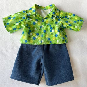 Peut inclure: Un ensemble pour poupée composé d'une chemise à manches courtes et d'un short. La chemise est verte avec un motif de pois bleus, jaunes et blancs. Le short est en denim bleu foncé. Un ensemble charmant.
