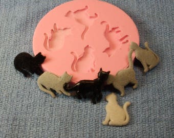 May include: A silicone mold for making cat-shaped decorations. The mold is pink and has five cat silhouettes. There are six finished cat decorations in various colors, including black, gray, and white.