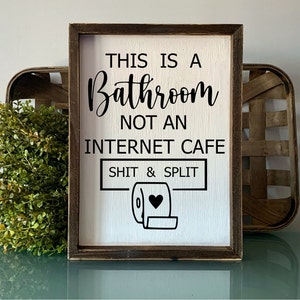 Peut inclure: Une pancarte en bois avec le texte "This is a Bathroom not an Internet Cafe Shit & Split" avec une icône de rouleau de papier toilette.