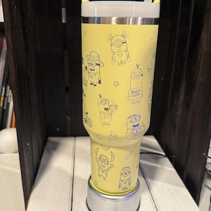 Pu&ograve; includere: Un bicchiere giallo con coperchio bianco e cannuccia trasparente, caratterizzato da un motivo ripetuto a linee nere di personaggi Minion e banane. Un Minion indossa un cappello, mentre un altro tiene un cartello con scritto I'M WITH STUPID.