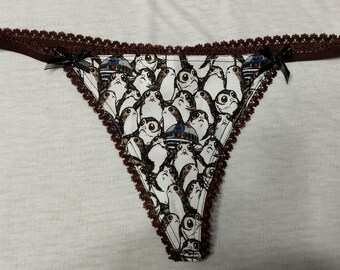 May include: White thong underwear with a repeating pattern of Porgs and Star Wars characters. The edges are trimmed with a dark brown lace and small black bows. A fun and unique addition to any wardrobe.