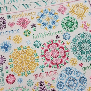 May include: Cross stitch pattern featuring a white background and colourful floral designs. The pattern includes the words "goodness", "faithfulness", "peace", and "joy".