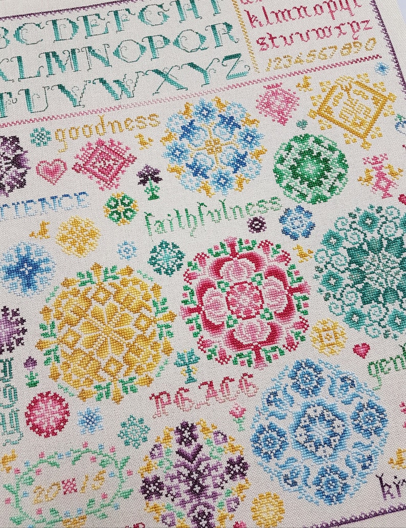 May include: Cross stitch pattern featuring a white background and colourful floral designs. The pattern includes the words "goodness", "faithfulness", "peace", and "joy".