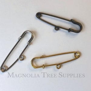 Peut inclure: Trois épingles de sûreté dans différentes finitions : or, argent et bronze. Les épingles sont toutes de la même taille et de la même forme, avec un design simple.