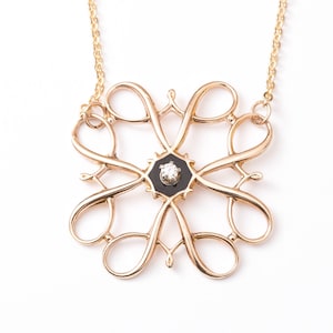 Pu&ograve; includere: Una collana d'oro con un ciondolo nero e bianco con un diamante al centro. Il ciondolo &egrave; un design delicato e intricato con pi&ugrave; anelli e volute.