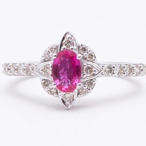 May include: A silver ring featuring a vibrant oval-cut pink gemstone at the center, surrounded by a halo of smaller, clear gemstones. The ring's band is also adorned with small, clear gemstones, creating a sparkling effect. A delicate and elegant piece of jewelry.