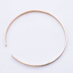 May include: A simple gold bangle bracelet with a hammered finish.