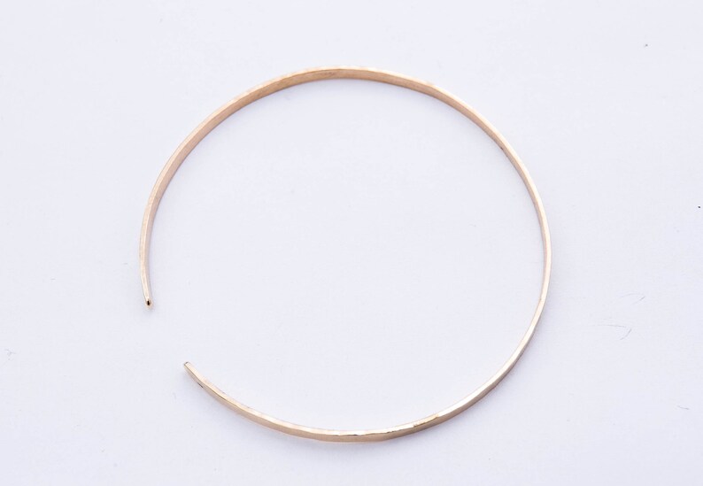 May include: A simple gold bangle bracelet with a hammered finish.