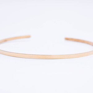 May include: A simple gold bangle bracelet, a thin band of metal with a smooth, polished finish.