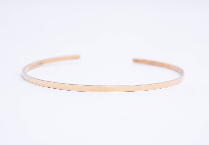 May include: A simple gold bangle bracelet, a thin band of metal with a smooth, polished finish.