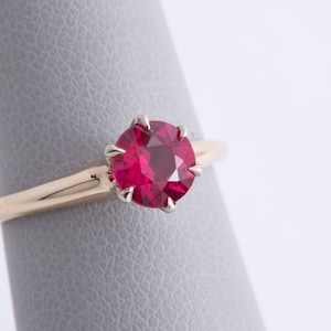May include: A gold ring with a red ruby gemstone set in a prong setting.