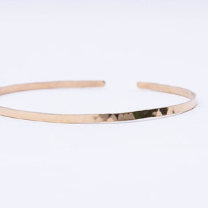 May include: A thin gold hammered bangle bracelet.