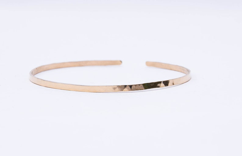 May include: A thin gold hammered bangle bracelet.