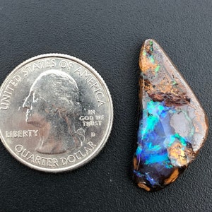 May include: A blue, green, and brown opal gemstone with iridescent flashes. The opal is about the size of a US quarter.