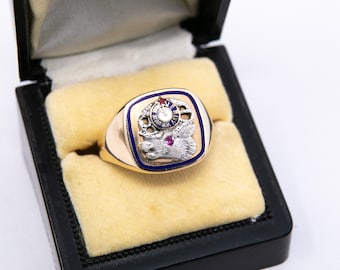 May include: A gold ring with a blue and white enamel design featuring a clock and a symbol. The ring is in a black velvet box.