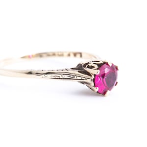 May include: A gold ring with a single, round, red gemstone set in a decorative, ornate setting.
