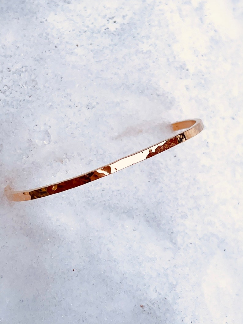May include: A thin, hammered gold bangle bracelet. The bracelet is simple and elegant, with a smooth, polished finish.