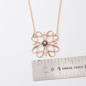 Pu&ograve; includere: Una collana con catena d'oro con un ciondolo con un designo in smalto nero con un piccolo diamante al centro. Il ciondolo ha un diametro di circa 2,5 cm.
