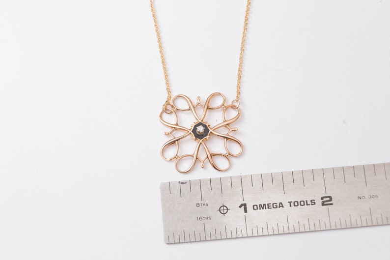 Pu&ograve; includere: Una collana con catena d'oro con un ciondolo con un designo in smalto nero con un piccolo diamante al centro. Il ciondolo ha un diametro di circa 2,5 cm.