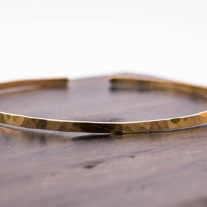 May include: A gold hammered bangle bracelet. The bracelet is thin and has a smooth, polished finish.