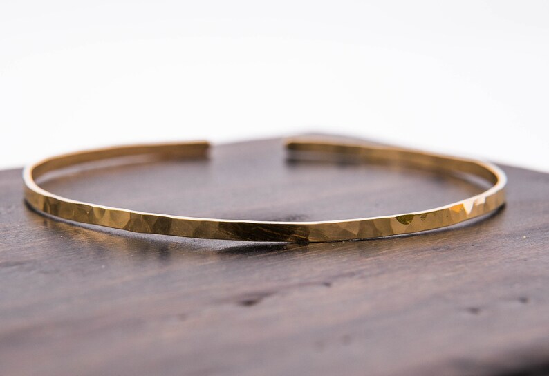 May include: A gold hammered bangle bracelet. The bracelet is thin and has a smooth, polished finish.