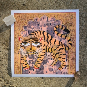 Peut inclure: Une illustration color&eacute;e d'un tigre marchant sous une pluie battante. Le tigre est repr&eacute;sent&eacute; dans un style indien traditionnel avec des d&eacute;tails complexes et des couleurs vives. L'arri&egrave;re-plan est une arche &agrave; motifs rose et or avec des gouttes de pluie tombant du ciel.