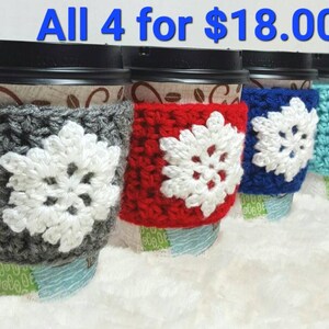 May include: Four coffee cups with black lids, each wrapped in a different colored crocheted cozy. The cozies are gray, red, blue, and turquoise, each with a white snowflake design. The text "All 4 for $18.00" is in the top of the image.