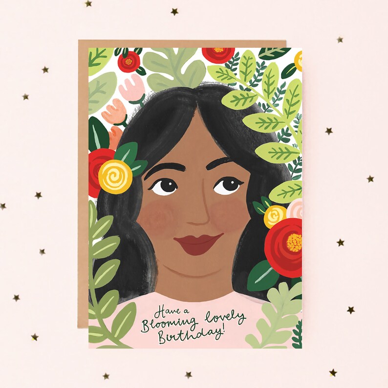 Puede incluir: Una tarjeta de cumplea&ntilde;os con una mujer de cabello negro largo rodeada de flores y vegetaci&oacute;n. El texto de la tarjeta dice "Have a Blooming Lovely Birthday!"