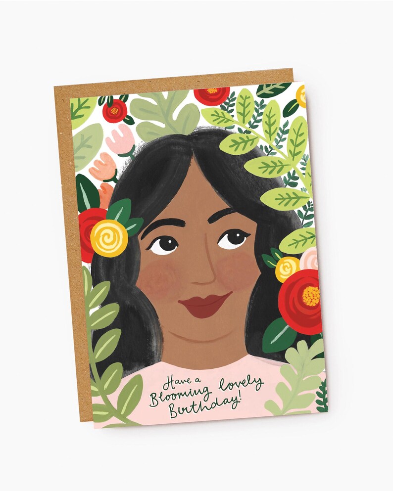 Puede incluir: Una tarjeta de cumplea&ntilde;os rosa con el rostro de una mujer rodeado de hojas verdes y flores rojas, amarillas y rosas. El texto de la tarjeta dice "Have a Blooming Lovely Birthday!"