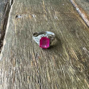May include: A silver ring with a large, square, pink gemstone set in a filigree design.