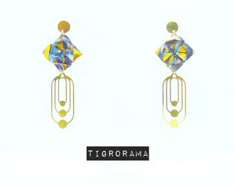 Könnte beinhalten: Ein Paar goldene geometrische Ohrringe mit einem quadratischen Anhänger in blau-gelber Musterung. Die Ohrringe haben eine Reihe von drei verbundenen Kreisen.
