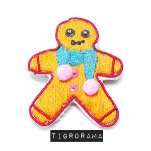 May include: An embroidered gingerbread man patch with a blue scarf, pink pom-poms, and gold sequins.