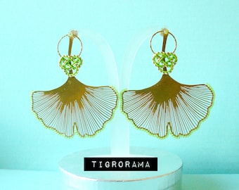 May include: Gold earrings with a ginkgo leaf design and a green knotted heart charm. The earrings are on a white display stand.