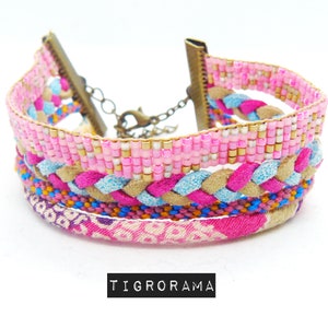 Puede incluir: Pulsera de múltiples capas con tejido tejido rosa, azul y marrón y cuentas. La pulsera tiene un cierre dorado.