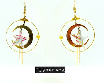May include: Gold earrings with a crescent moon and a white origami star with pink and yellow accents. The earrings have a dangling chain.