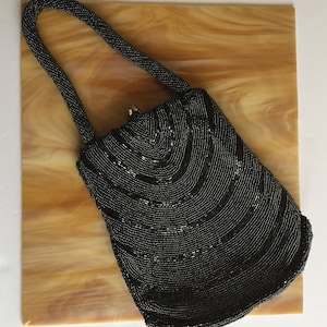 Peut inclure: Un sac &agrave; main de soir&eacute;e noir en perles avec un design incurv&eacute; et une poign&eacute;e sup&eacute;rieure.